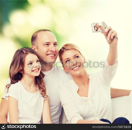 family, technology, ecology and people - smiling mother, father and little girl making selfie with camera over green background