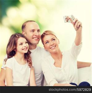 family, technology, ecology and people - smiling mother, father and little girl making selfie with camera over green background