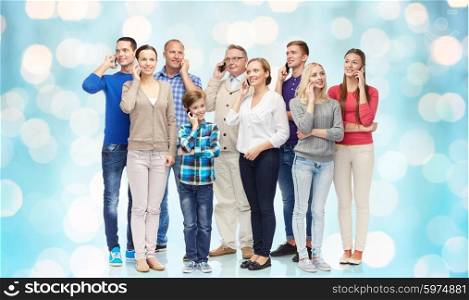 family, technology, generation and people concept - group of smiling men, women and boy with smartphones calling over blue holidays lights background