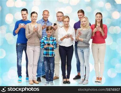 family, technology, generation and people concept - group of smiling men, women and boy with smartphones over blue holidays lights background