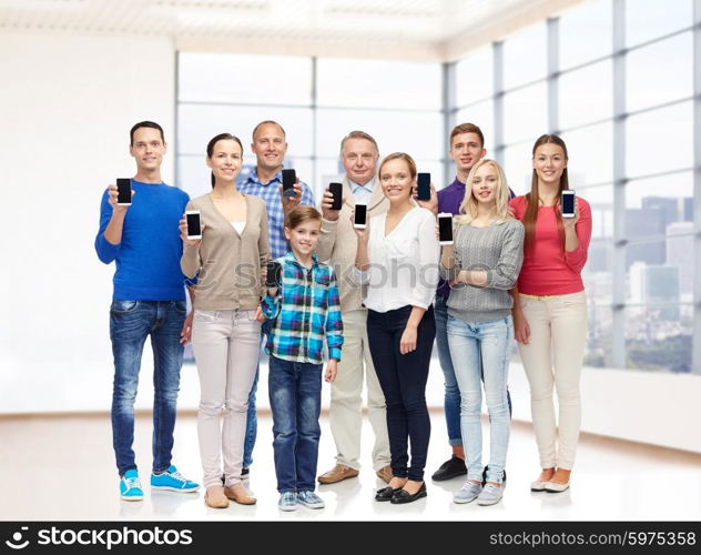 family, technology, generation and people concept - group of smiling men, women and boy with smartphones over empty office room or home