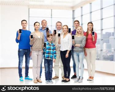family, technology, generation and people concept - group of smiling men, women and boy with smartphones over empty office room or home