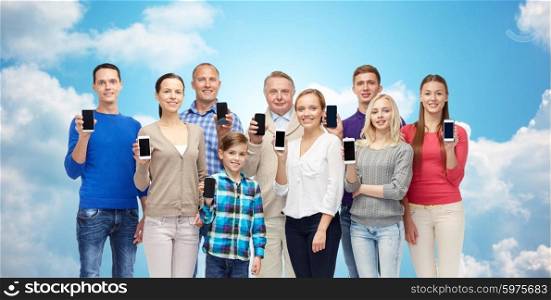 family, technology, generation and people concept - group of smiling men, women and boy with smartphones over blue sky and clouds background