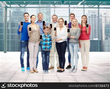 family, technology, generation and people concept - group of smiling men, women and boy showing smartphones over terminal with window city view background