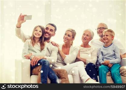 family, technology, generation and people concept - happy family sitting on couch and making selfie with smartphone at home