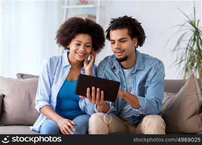 family, technology, internet and people concept - happy couple with tablet pc computer and earphones listening to music at home. happy couple with tablet pc and earphones at home