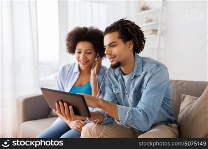 family, technology, internet and people concept - happy couple with tablet pc computer and earphones listening to music at home. happy couple with tablet pc and earphones at home