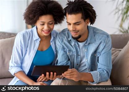 family, technology, internet and people concept - happy couple with tablet pc computer and earphones listening to music at home. happy couple with tablet pc and earphones at home. happy couple with tablet pc and earphones at home