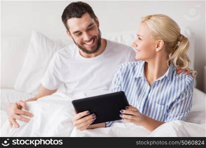 family, technology, internet and people concept - smiling happy couple with tablet pc computer in bed at home bedroom. smiling happy couple with tablet pc in bed at home