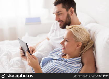 family, technology, internet and people concept - smiling happy couple with tablet pc computer in bed at home bedroom. smiling happy couple with tablet pc in bed at home