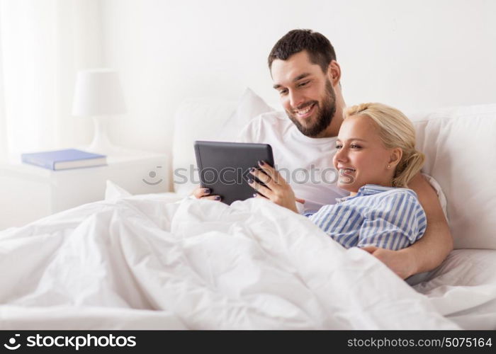 family, technology, internet and people concept - smiling happy couple with tablet pc computer in bed at home bedroom. smiling happy couple with tablet pc in bed at home