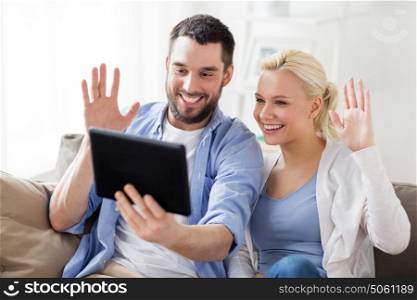 family, technology, internet, online communication and people concept - smiling happy couple with tablet pc computer having video chat and waving hands at home. couple with tablet pc having video chat at home