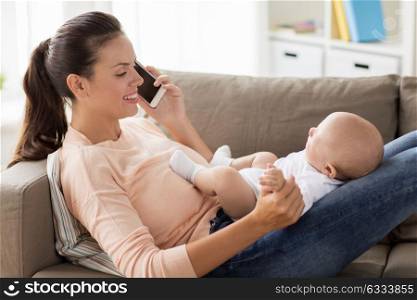 family, technology, motherhood and people concept - happy mother with little baby boy lying on sofa and calling on smartphone at home. mother with baby calling on smartphone at home