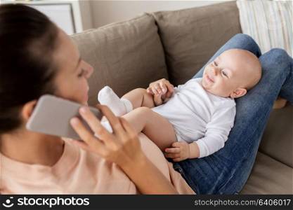 family, technology, motherhood and people concept - happy mother with little baby boy lying on sofa and calling on smartphone at home. mother with baby calling on smartphone at home