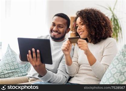 family, technology, online shopping and people concept - happy african american couple couple with tablet pc computer and credit card at home. couple with tablet pc and credit card at home