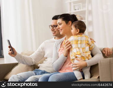 family, technology, parenthood and people concept - happy mother and father showing tablet pc computer to baby daughter at home. mother, father and baby with tablet pc at home