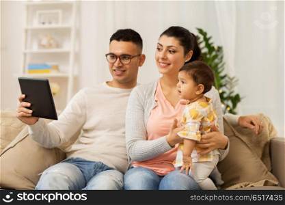 family, technology, parenthood and people concept - happy mother and father showing tablet pc computer to baby daughter at home. mother, father and baby with tablet pc at home. mother, father and baby with tablet pc at home