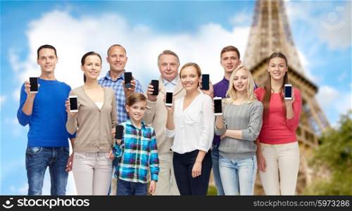 family, technology, travel and tourism concept - group of smiling people with smartphones over eiffel tower background