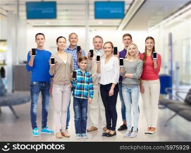 family, technology, travel and tourism concept - group of smiling people with smartphones over airport waiting room background