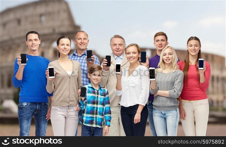 family, technology, travel and tourism concept - group of smiling people with smartphones over coliseum background