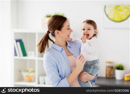 family, teething, motherhood and people concept- happy mother and little baby girl at home kitchen. happy mother and little baby girl at home kitchen