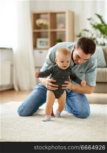 family, toddling and fatherhood concept - father helping little baby daughter with walking at home. father helping baby daughter with walking at home
