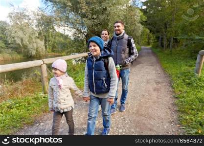 family, tourism and hiking concept - happy mother, father, son and daughter with backpacks walking in woods. family with backpacks hiking or walking in woods