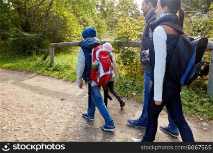 family, tourism and hiking concept - happy mother, father, son and daughter with backpacks walking in woods. family with backpacks hiking or walking in woods. family with backpacks hiking or walking in woods