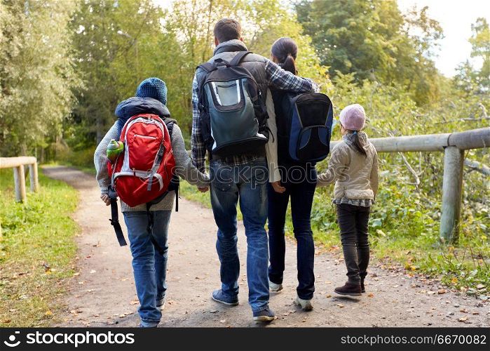 family, tourism and hiking concept - happy mother, father, son and daughter with backpacks walking in woods. family with backpacks hiking or walking in woods. family with backpacks hiking or walking in woods