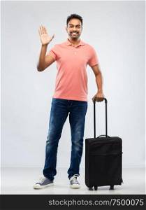 family, tourism and vacation concept - smiling indian man in polo shirt with travel bag waving hand over grey background. smiling indian man with travel bag waving hand