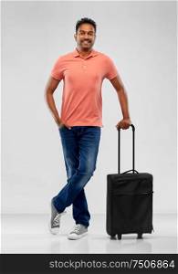 family, tourism and vacation concept - smiling indian man in polo shirt with travel bag over grey background. smiling indian man in polo shirt with travel bag