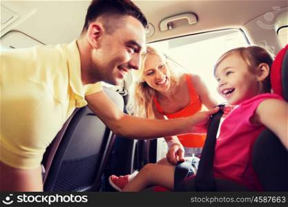 family, transport, road trip and people concept - happy parents fastening child with safety belt in baby car seat