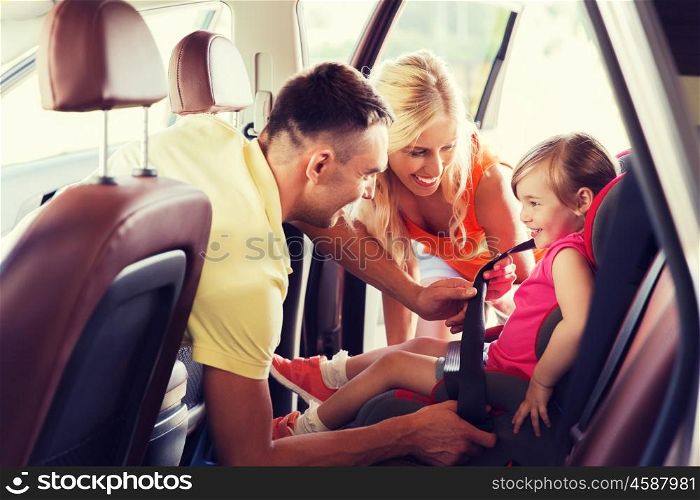 family, transport, road trip and people concept - happy parents fastening child with safety belt in baby car seat