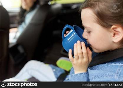 family, transport, road trip and people concept - little girl driving in car with mother and drinking from cup