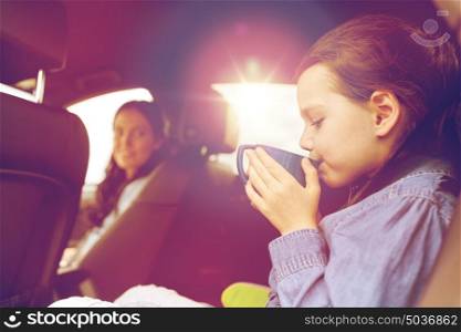 family, transport, road trip and people concept - little girl driving in car with mother and drinking from cup. little girl driving in car and drinking from cup