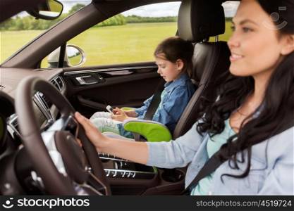 family, transport, road trip, travel and people concept - happy woman and little daughter with smartphone driving in car