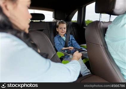 family, transport, road trip, travel and people concept - happy woman giving tablet pc computer to little daughter in car