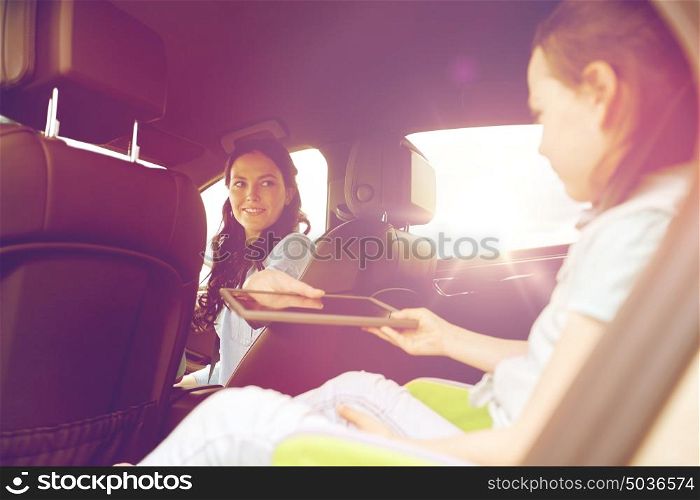 family, transport, road trip, travel and people concept - happy woman giving tablet pc computer to little daughter in car. happy family with tablet pc driving in car