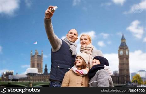 family, travel and tourism concept - happy mother, father, daughter and son taking selfie by camera over big ben tower in london city background. family taking selfie by camera over london city