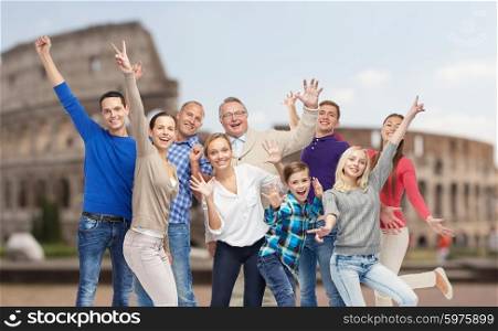 family, travel, tourism and people concept - group of happy men, women and boy having fun and waving hands over coliseum background