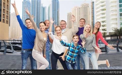 family, travel, tourism and people concept - group of smiling men, women and boy having fun and waving hands over dubai city street background