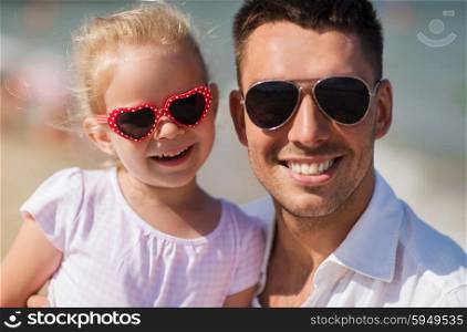 family, travel, vacation, adoption and people concept - happy father with little girl in sunglasses on summer beach