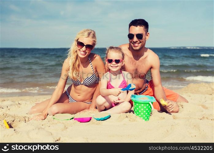 family, travel, vacation and people concept - happy man, woman and little girl in sunglasses playing with sand toys on summer beach