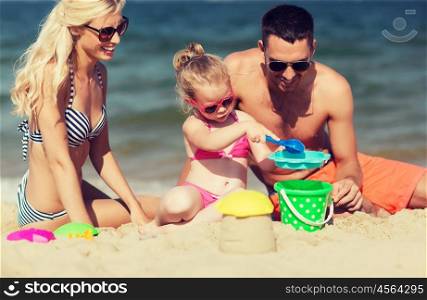 family, travel, vacation and people concept - happy man, woman and little girl in sunglasses playing with sand toys on summer beach