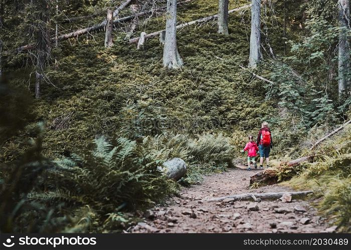 Family trip close to nature. Mother with little girl walking on path in forest, actively spending summer time together