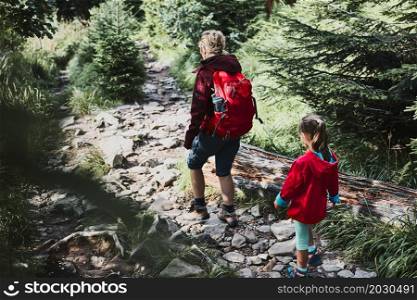Family trip in mountains. Mother with little girl walking on path in forest, actively spending summer time together. Enjoying the outdoors in the summer trip vacation