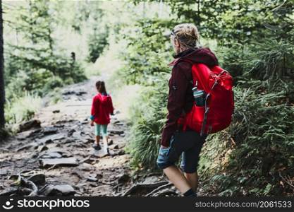 Family trip in mountains. Mother with little girl walking on path in forest, actively spending summer time together. Enjoying the outdoors in the summer trip vacation