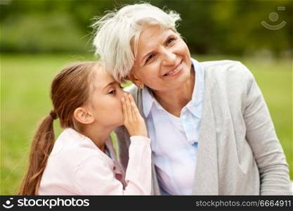 family, trust and people concept - happy granddaughter whispering secrets to grandmother at summer park. granddaughter sharing secrets with grandmother