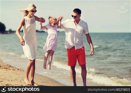 family, vacation, adoption and people concept - happy man, woman and little girl in sunglasses walking on summer beach