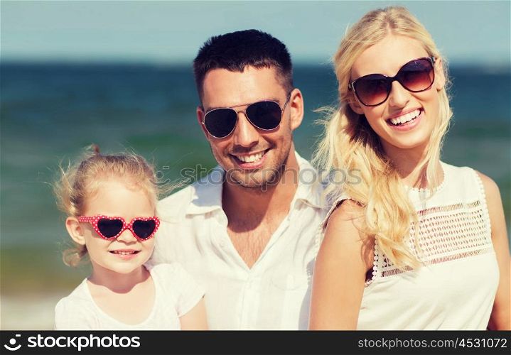 family, vacation, adoption and people concept - happy man, woman and little girl in sunglasses on summer beach